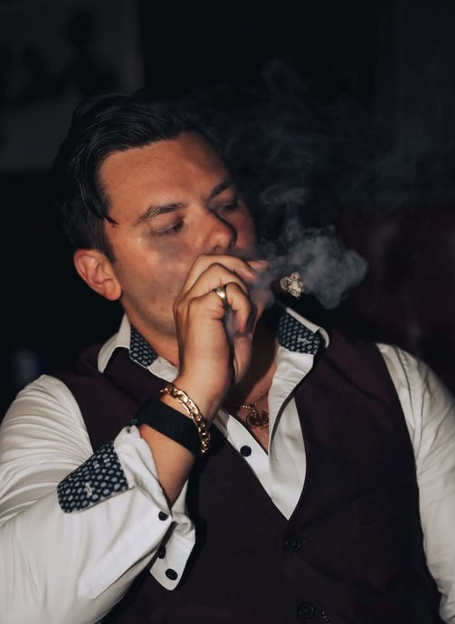 A member exhaling cigar smoke in a waistcoat