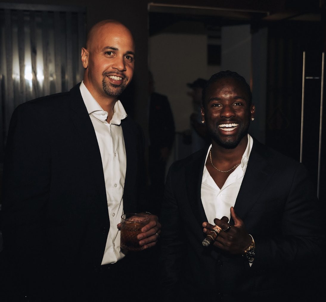 Two members sharing a laugh with cigars and drinks